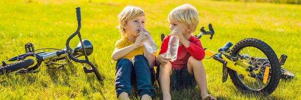 Two little boys drink water in the park after riding a bike BANNER, LONG FORMAT - Fotografie, Obrázek