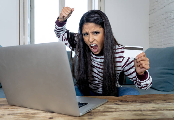 Vonzó fiatal latin nő elkeseredett és dühös hitelkártya és a laptop elhelyezés kanapén otthon hitelkártya problémák adósságok online fizetés online vásárlás online banki a rossz pénzügyi helyzete. - Fotó, kép
