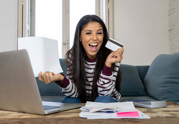 Cheerful attractive latin woman using credit card calculator and laptop paying bills at home looking relax in home finances paying bills online banking buying online and internet shopping. - Photo, Image
