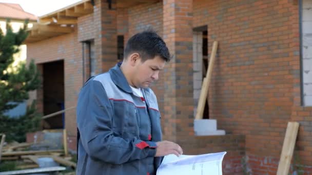 Dorosły człowiek patrząc na papierze plany stojący na zewnątrz budynku w budowie - Materiał filmowy, wideo