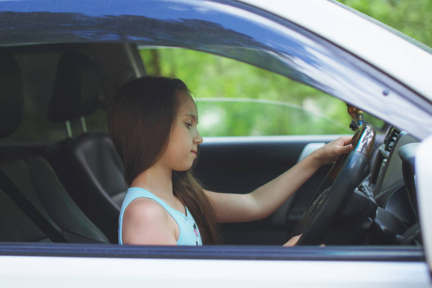 Nastolatek dziewczyna z długimi włosami siedzi za kierownicą samochodu. - Zdjęcie, obraz