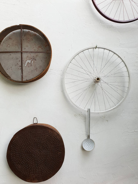 Peneiras, rodas de bicicleta e uma concha pendurada em uma parede branca de uma casa tradicional de Lefka Chipre para fins de decoração
 - Foto, Imagem