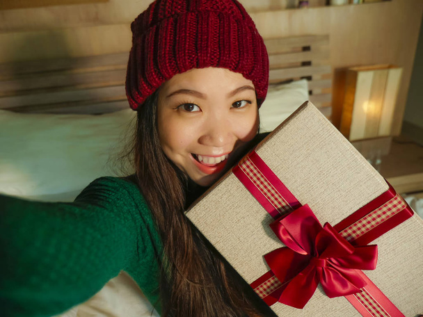 giovane bella e felice donna asiatica americana scattare foto selfie con cellulare in possesso di scatola regalo di Natale sorridente allegro ed eccitato in inverno beamy a casa festeggiando le vacanze di Natale
 - Foto, immagini