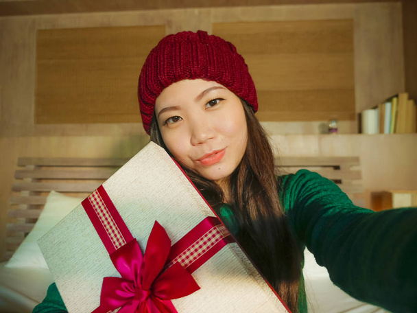 jeune belle et heureuse femme coréenne asiatique prenant selfie photo avec téléphone portable tenant boîte cadeau de Noël souriant gai et excité en hiver beamy à la maison célébrant les vacances de Noël
 - Photo, image