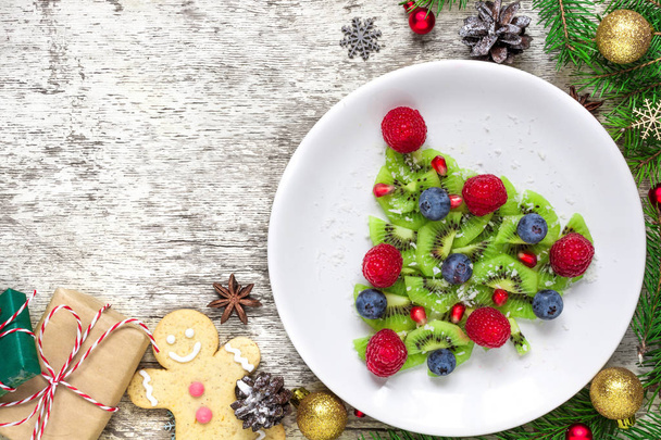 Kiwi vánoční strom s větvemi stromu jedle a dárkové krabice nad bílý dřevěný stůl. Funny potravin nápad pro děti. Vánoční a novoroční jídlo pozadí. pohled shora s kopií prostor - Fotografie, Obrázek