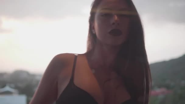 Πορτρέτο της σέξι μελαχρινή γυναίκα στο μαύρο σουτιέν που παρουσιάζουν εξωτερική συννεφιασμένο ουρανό φόντο. Θέα από το εσωτερικό του διαμερίσματος μέσω του παραθύρου βεράντα - βίντεο σε αργή κίνηση - Πλάνα, βίντεο