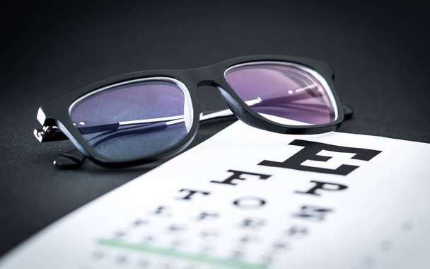 目の試験と視力試験のコンセプトです。文字チャートのメガネ。テーブルの上の眼鏡。眼科で視力と視野検査。検眼や眼鏡. - 写真・画像