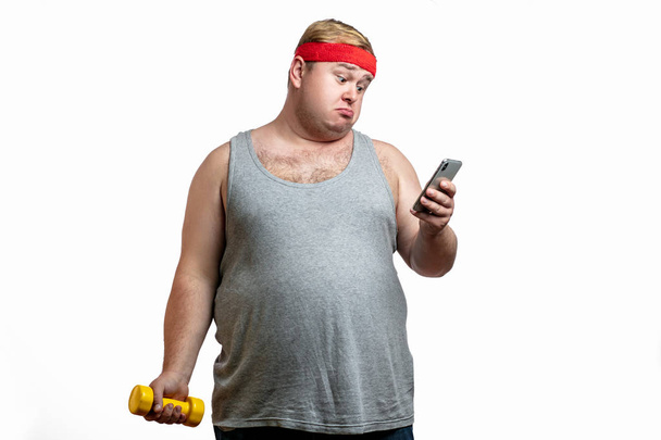 Waist-up shot of displeased gloomy obese male fatso in casual t-shirt, staring disappointed at camera, frowning and expressing dislike, looking at smartphone - Φωτογραφία, εικόνα
