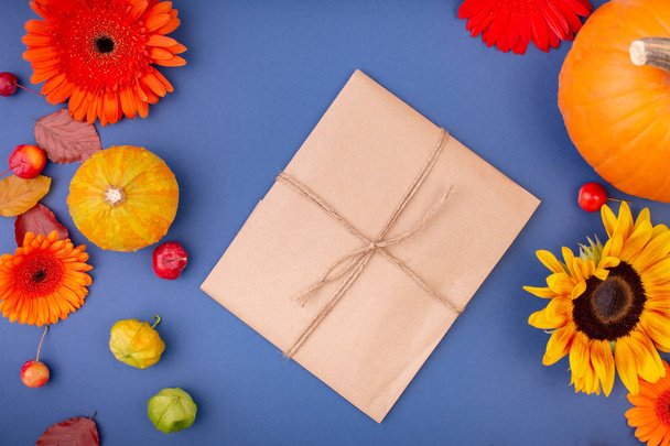 Vista superior de la caja de regalo artesanal con flores y calabazas amarillas y anaranjadas sobre fondo azul. Tarjeta de felicitación en blanco para el diseño creativo del trabajo. plano laico
 - Foto, Imagen