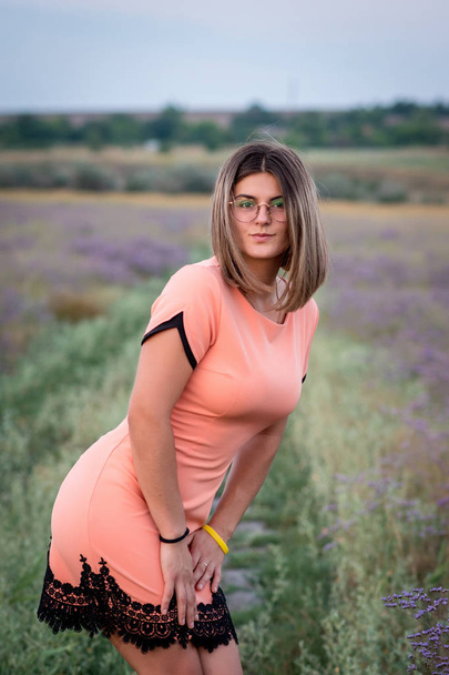 Дівчина в короткій сукні в персиковому кольорі, стоїть нахиляючись вперед
 - Фото, зображення
