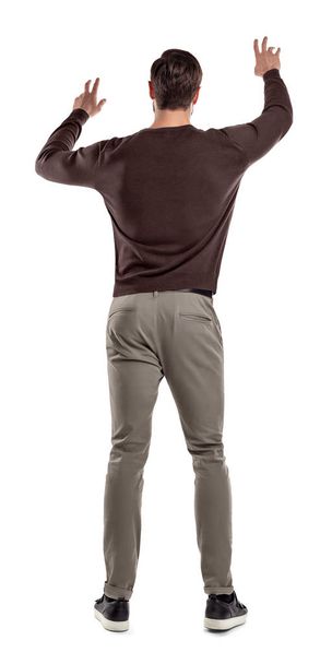 A fit man in casual sweater stands in a back view with both arms lifted up to manipulate an invisible touch screen. - Foto, Bild