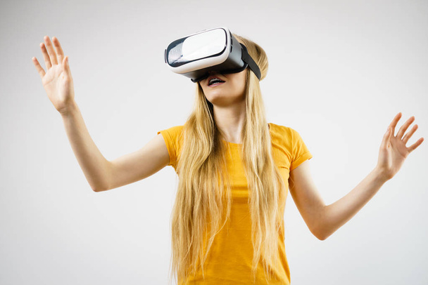 Young woman wearing virtual reality goggles headset, vr box, stretching arms. Connection, technology, new generation and progress concept. Studio shot on gray - Photo, Image