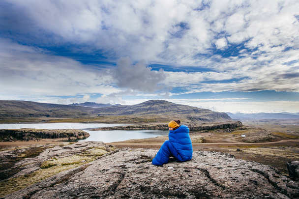 Jovem mulher em saco de dormir azul quente, nas pedras com massa do norte, Islândia
 - Foto, Imagem