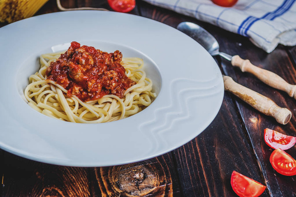Tradycyjny włoski makaron spaghetti bolognesse z mięsa mielonego i pomidory i surowego spaghetti na ciemny stół z drewna - Zdjęcie, obraz