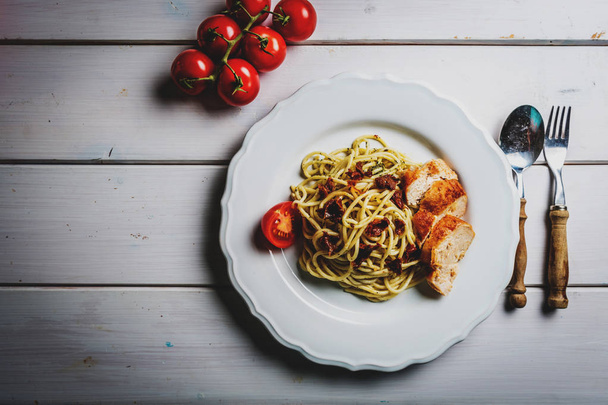 Spaghetti di pasta italiana con pollo, pomodoro essiccato e pesto di basilico su tavola bianca
 - Foto, immagini