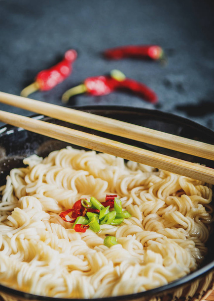 Черная миска азиатской лапши с горячей водой и красным перцем чили и зеленым луком и палочками для еды
 - Фото, изображение