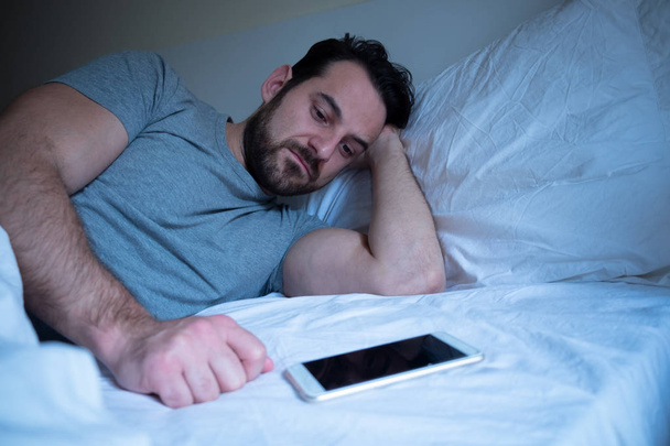 Θλιβερή τύπος περιμένουν ένα τηλεφώνημα ξαπλωμένη στο κρεβάτι - Φωτογραφία, εικόνα