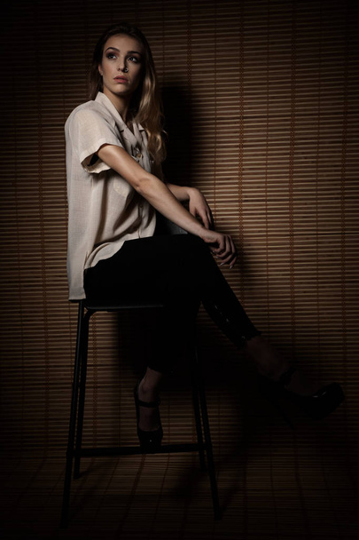 Mulher jovem na moda senta-se em uma cadeira com parede de madeira no fundo
 - Foto, Imagem