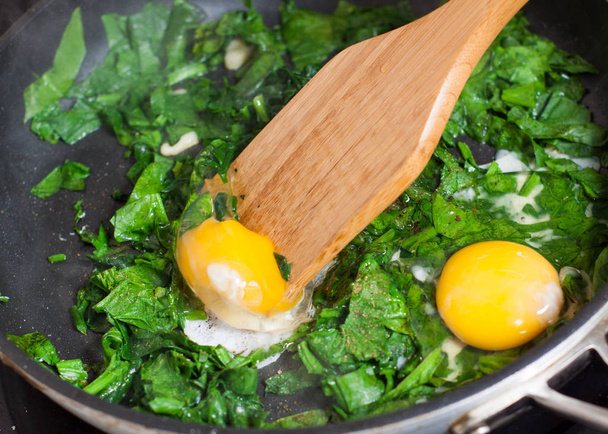 Preparazione di uova strapazzate con spinaci - aggiungere l'uovo alle foglie di spinaci
 - Foto, immagini