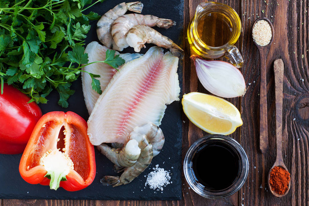 Grondstoffen voor zeevruchten schotel - tilapia filets, garnalen, rode paprika, ui, citroen, kruiden, olijfolie en sojasaus - Foto, afbeelding