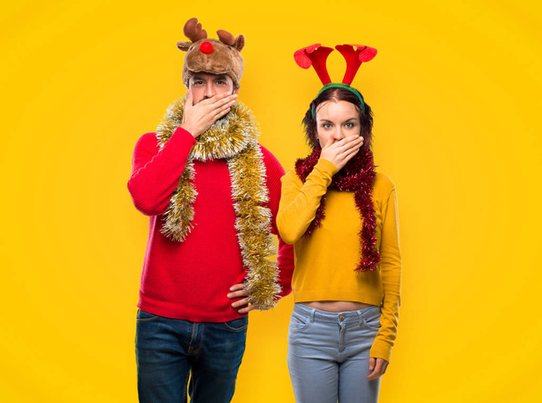 Couple habillé pour les vacances de Noël couvrant la bouche avec les mains pour dire quelque chose d'inapproprié sur fond jaune
 - Photo, image