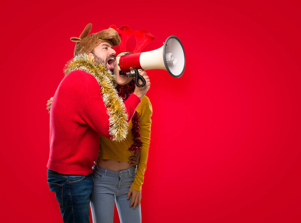 Пара, одягнена на різдвяні свята, тримає мегафон на ізольованому червоному тлі
 - Фото, зображення