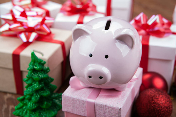Piggy bank egy rózsaszín ajándék doboz, a háttérben a karácsonyi játékok és díszdobozok - Fotó, kép
