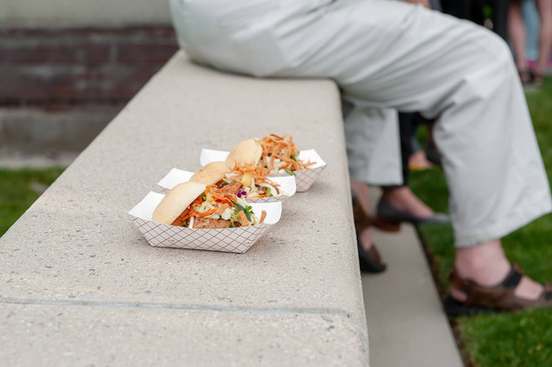 Three sandwiches in to-go cartons on a concrete ledge with fellow eaters in the background. - Photo, Image