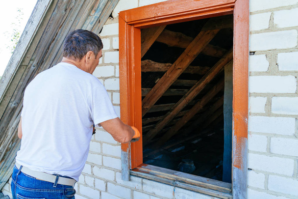 Чоловік малює обробку навколо пензлем, малюючи дерев'яне вікно зовні
 - Фото, зображення
