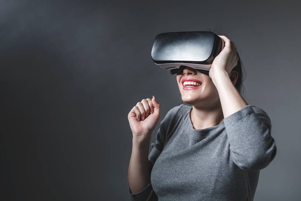 Young woman using a virtual reality headset on a gray background - Fotoğraf, Görsel