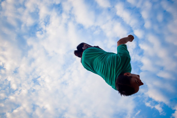 Взрослый парень делает сальто назад под голубым небом
 - Фото, изображение