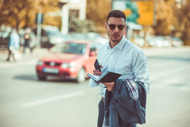 Hombre de negocios guapo está en la ciudad, hablando y caminando por la calle, sosteniendo un cuaderno en sus manos
 - Foto, imagen