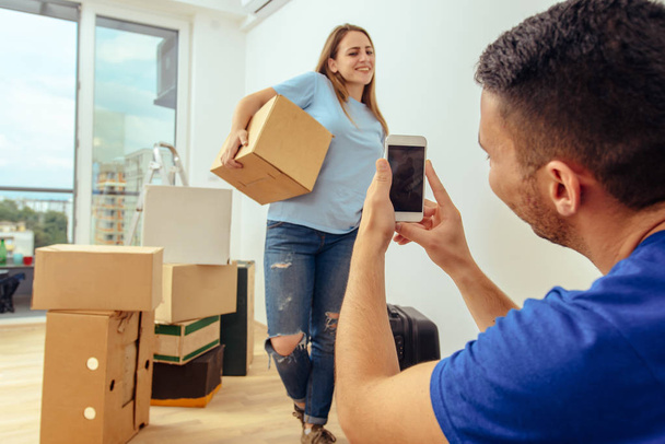Guy picture his girlfriend while holding cardboard box in living room - Fotografie, Obrázek
