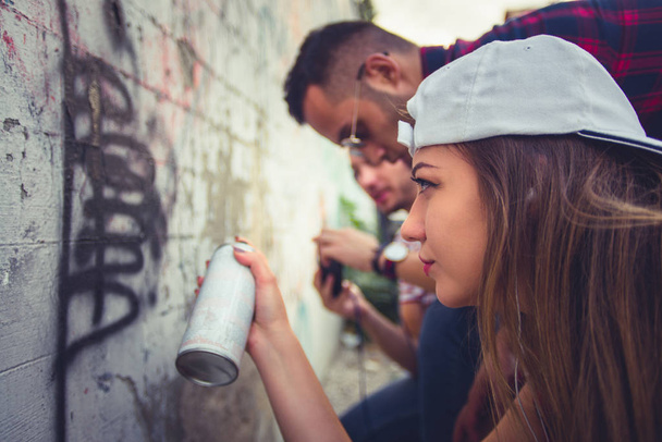 Three urban people are having fun together, drawing grafitii on the wall - Foto, immagini