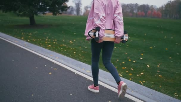 Young pretty beautiful blond hipster woman walking down the road with skateboard longboard in slow motion - Video, Çekim