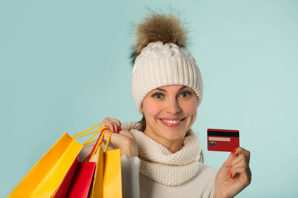 beautiful young girl in winter hat with packages and credit card in hands on a blue background - Photo, image