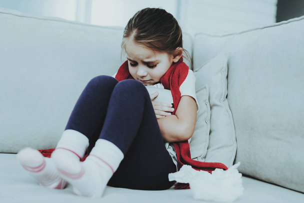 Little Girl with Cold Sitting on Sofa in Red Scarf. Sick Young Girl. White Sofa in Room. Unhappy Child. Disease Concept. Healthcare and Healthy Lifestyle Concept. Little Girl at Home. - Фото, зображення