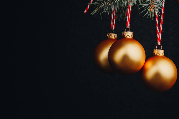 christmas and new year gift-card. branches of fir-tree and decoration with golden balls on a black background isolated close up - Foto, imagen