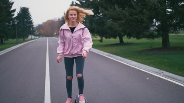Joven hermosa rubia hipster mujer en rosa windstopper divertirse montar monopatín longboard cuesta abajo en hermosa carretera en cámara lenta
 - Metraje, vídeo