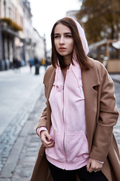 young woman in brown coat and pink hoody posing on the street - Foto, Imagem