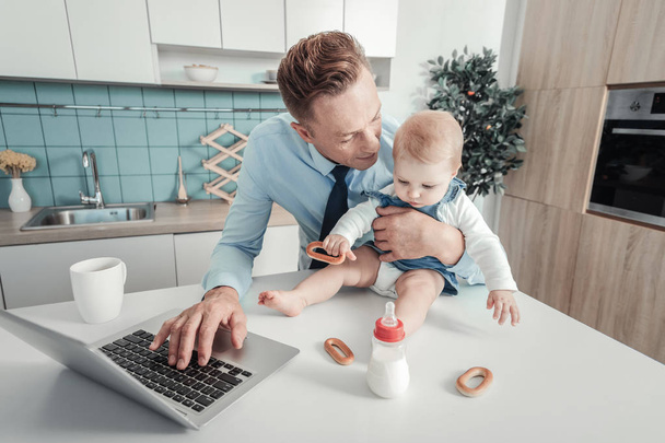 Caring lovely father using the laptop looking at baby. - Фото, изображение