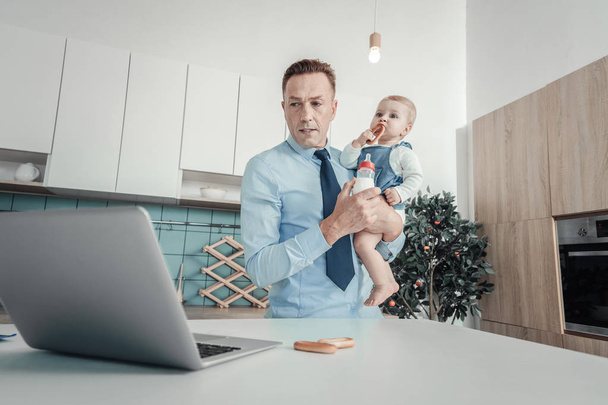 Serious concentrated man standing and holding a baby. - Photo, image