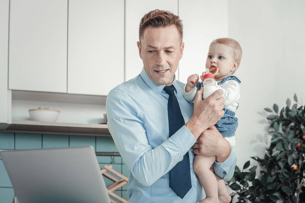 Занятый сосредоточенный мужчина держит ребенка дома
. - Фото, изображение