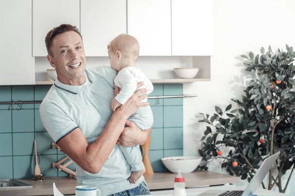 Joyful handsome man smiling and holding a baby. - 写真・画像