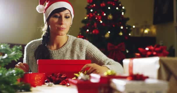 Girl with Christmas hat makes wishes and opens a Christmas gift package. concept of holidays and new year. the girl is happy and smiles with christmas gift in hand. - Кадры, видео