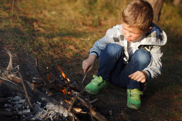 Boy in a plaid shirt make a fire in the autumn forest. - Zdjęcie, obraz