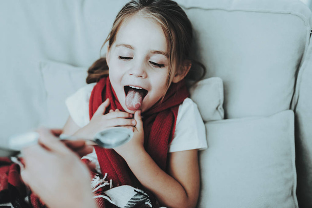 Little Girl with Cold Sitting on Sofa in Red Scarf. Medicinal Syrup. Sick Young Girl. White Sofa in Room. Unhappy Child. Disease Concept. Healthcare and Healthy Lifestyle Concept. Little Girl at Home. - Foto, Imagem