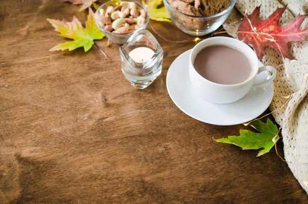 Šálek horkého kakaa, ořechů, sušenek, svíček a pletených kostek na venkovském dřevěném stole. Útulná podzimní nálada, teplý podzim. - Fotografie, Obrázek