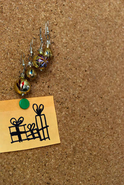 ondo de corcho marrn con esferitas doradas navideas y dibujo en postit de regalos navideos en vertical  - Foto, immagini