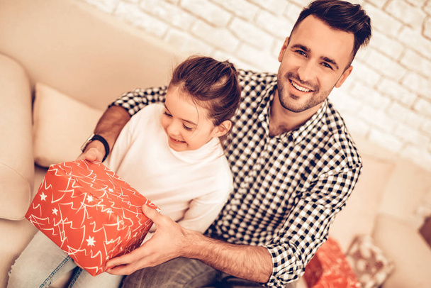 Father and Daughter on Sofa. Spend Time Together. Father's day. Man Play with Girl. Smiling Girl at Home. Sit on Sofa. Gift box. Gift in Red Pack. Man with Gift for Child. Make Surprise for Daughter. - Foto, Imagem